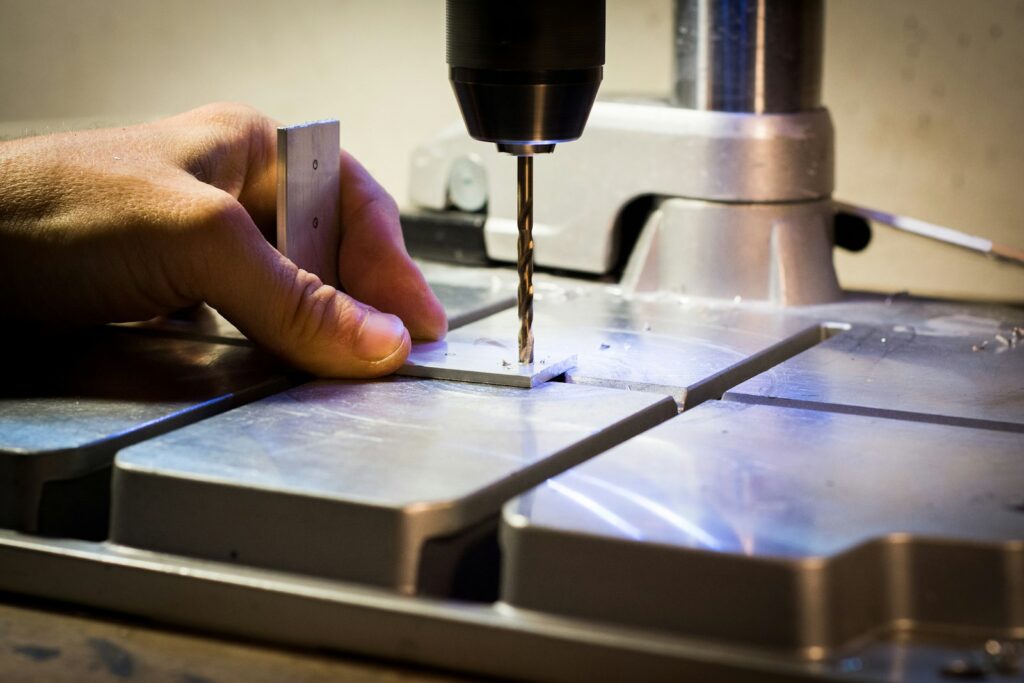 Operator's hand guiding a drilling machine as it drills into a metal bar